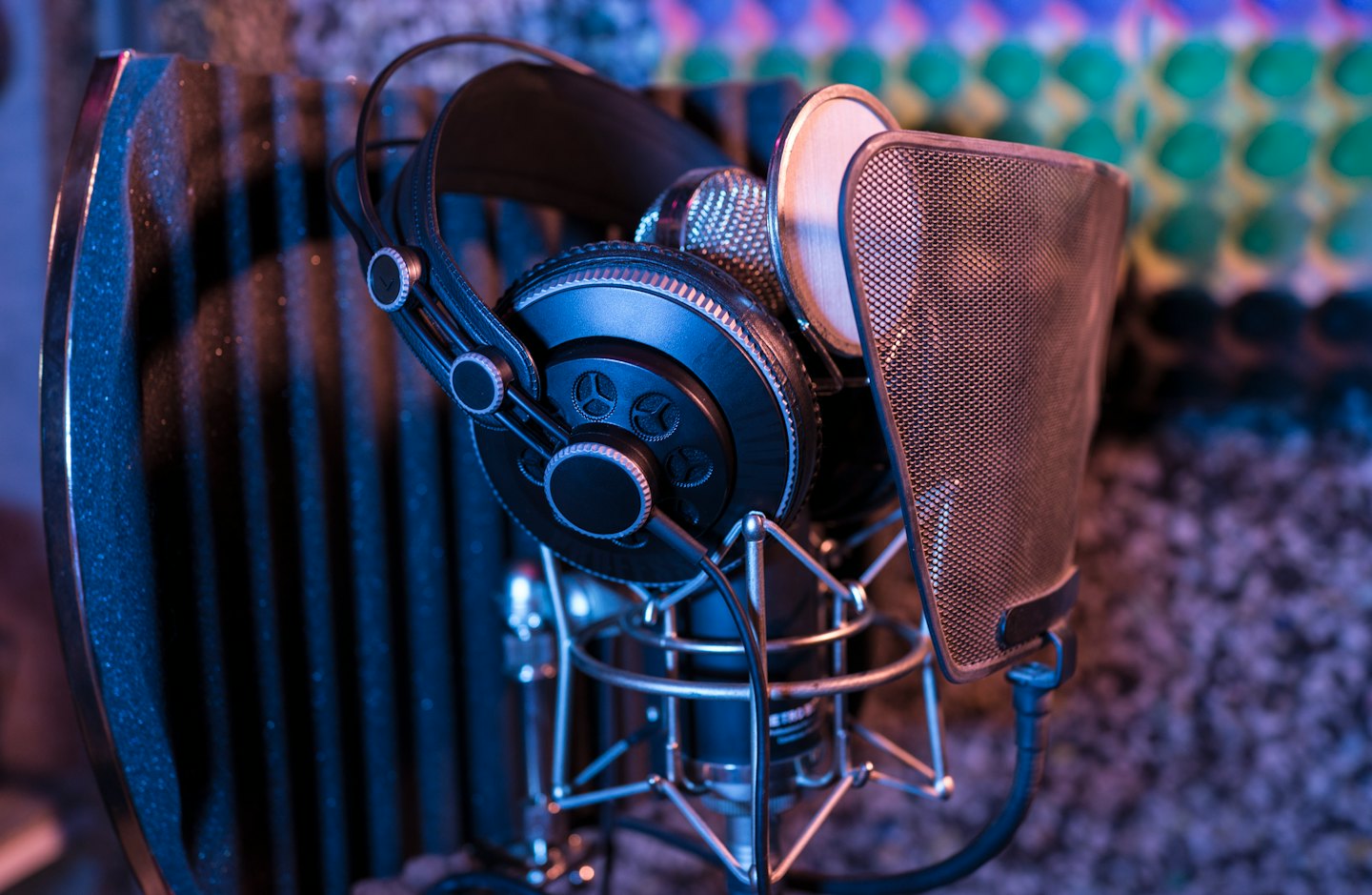 Black headphones sit on a silver microphone in a recording studio.